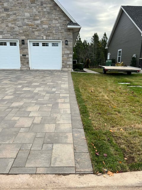 Residential driveway with paver stones leading to a brick house with two white garage doors