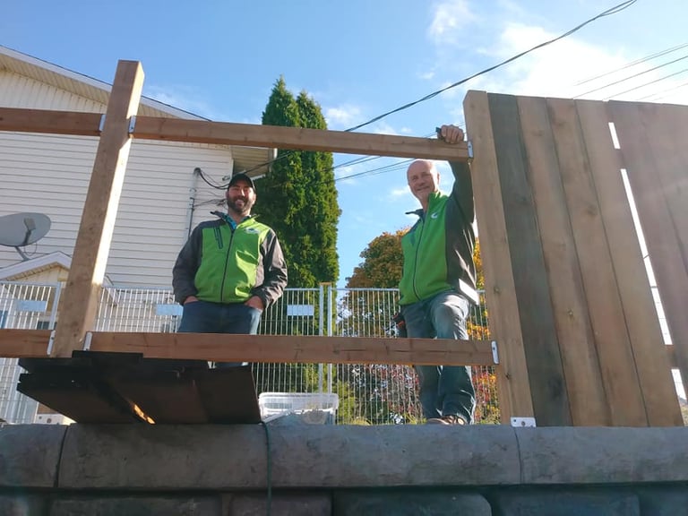 Two construction workers in green vests standing on wooden beams at a residential building site.