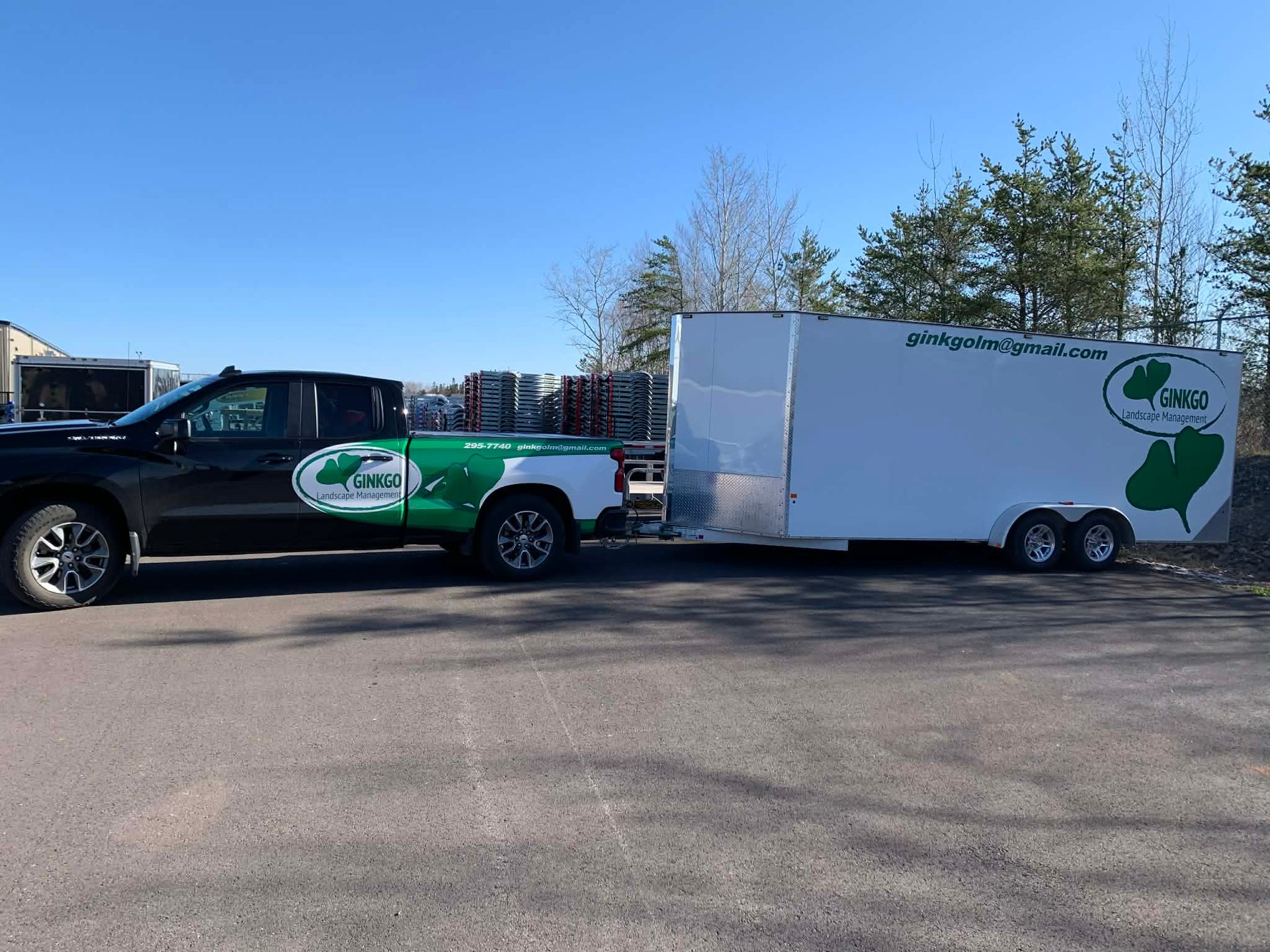 Black pickup truck towing a white enclosed trailer with green logo branding in a parking lot