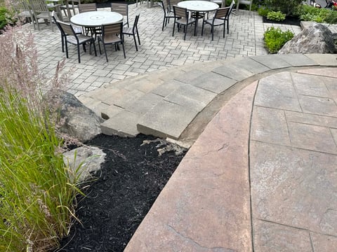 Outdoor patio with paver seating areas, decorative black mulch bed with ornamental grasses, and dining sets in background