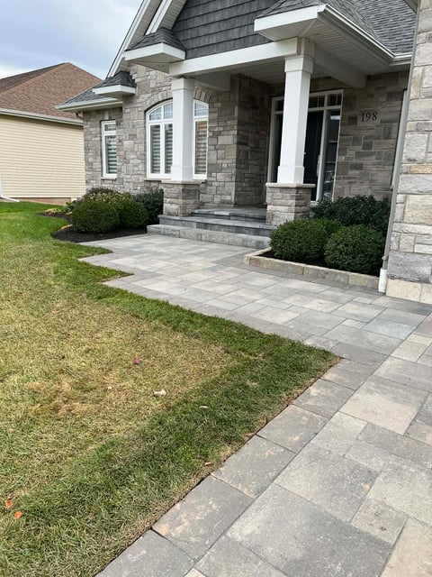 Modern home exterior with stone facade, white columns, paved walkway, manicured lawn and foundation plantings