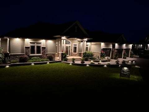 Modern single-story house illuminated at night with landscaped lawn, stone accents, and decorative outdoor lighting