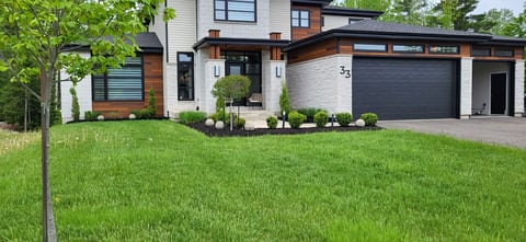 Modern residential home with mixed materials, garage, and manicured lawn surrounded by green trees